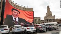 Vehicles stand in a parking lot as a large screen shows an image of Chinese President Xi Jinping in Kashgar, Xinjiang autonomous region, China, on Thursday, November 8, 2018.